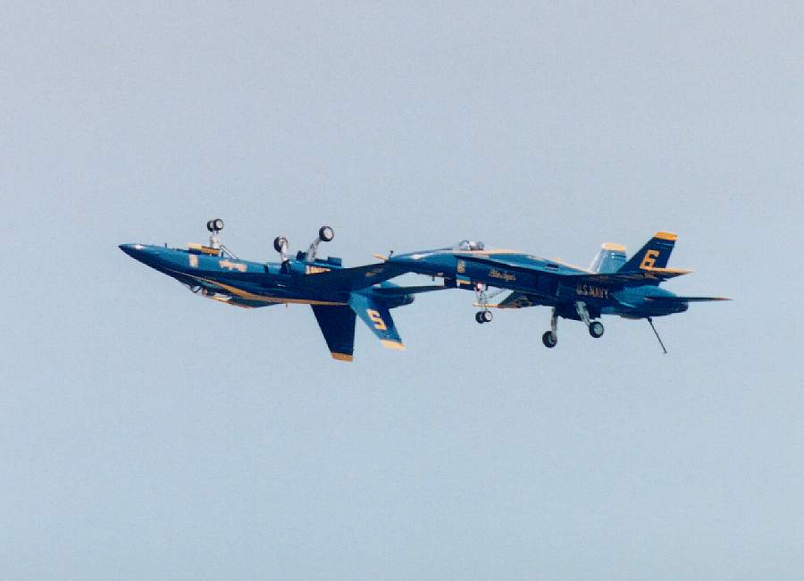 two Blue Angels flying side-by-side with wheels extended, one plane upright and one inverted