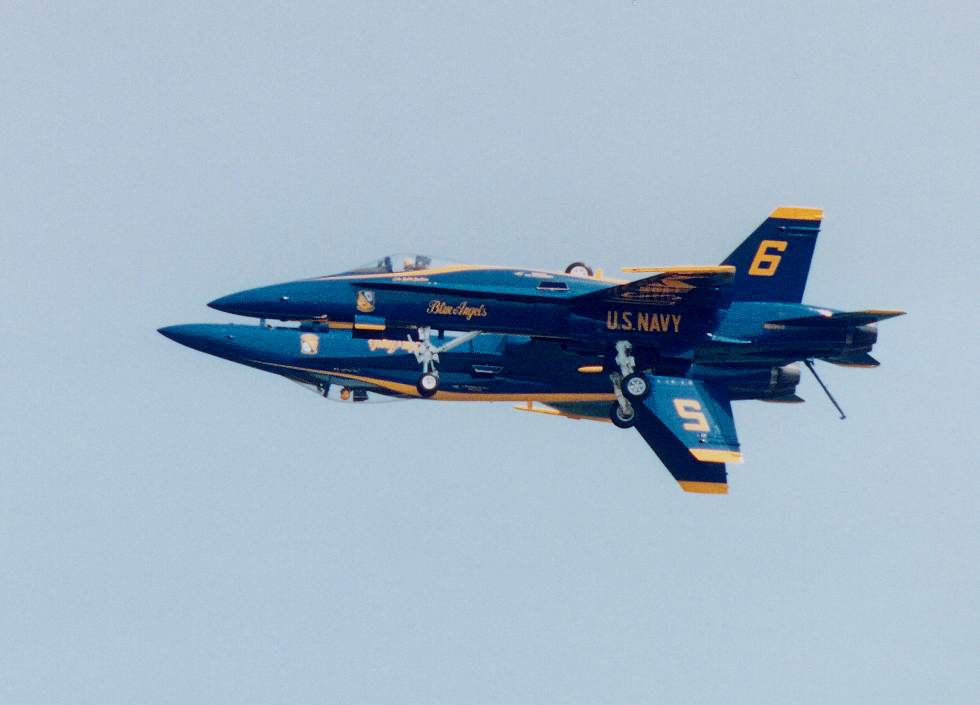 two Blue angels flying side-by-side with wheels extended, one upright and one inverted