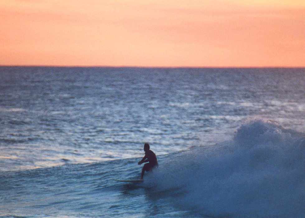 sunset begins as the surfer rides out his wave