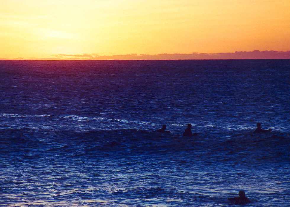 surfers sit on the water as the light runs out