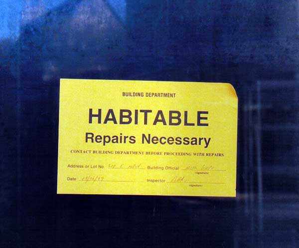 sign pasted on window reading Habitable, repairs necessary