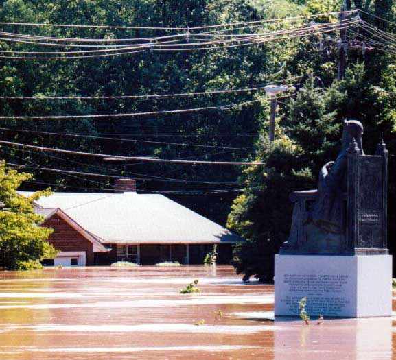 Statue of a seated woman at the local Ukrainian Orthodox church, surrounded by water and across from a flooded house.