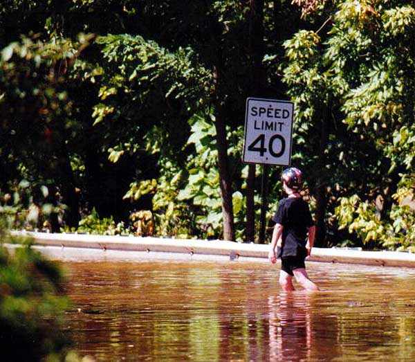 Kid walking down Canal Road in knee deep water.